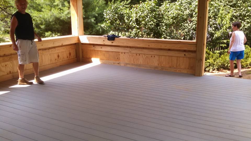 Two people stand on a wide, wooden deck with gray composite flooring under a covered patio structure.