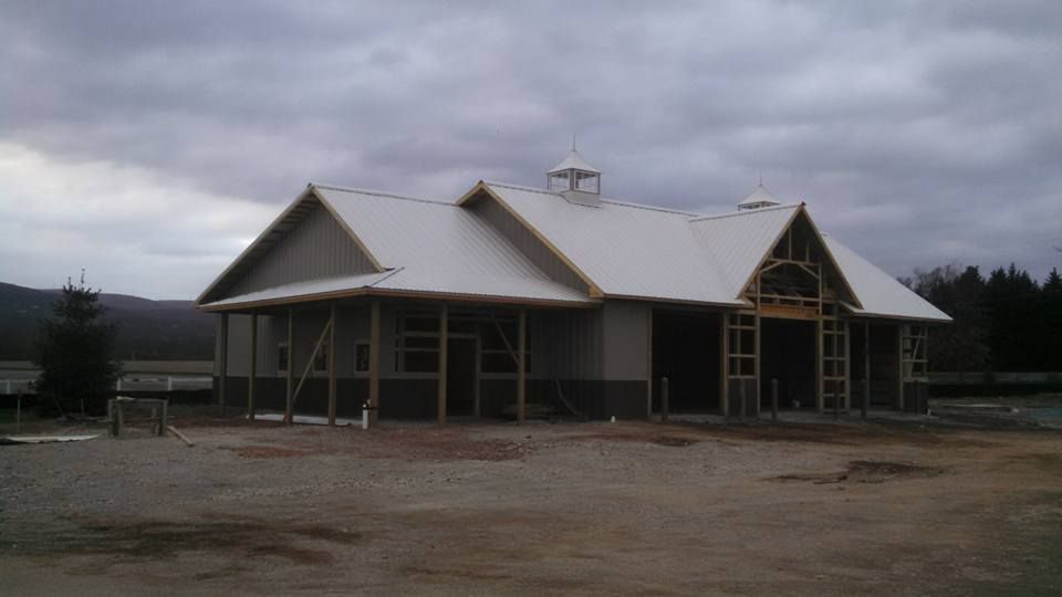 A large, partially constructed building with a white metal roof, two cupolas, and a porch under a cloudy sky.