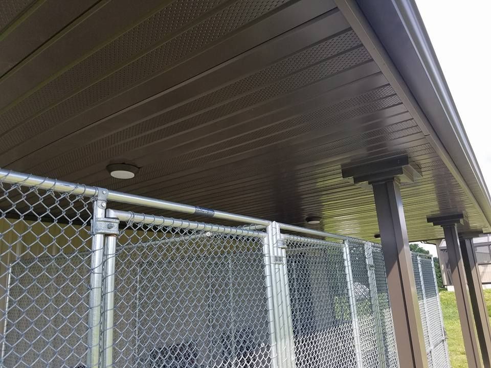 A dark brown horizontal paneled ceiling overhang covers a chain-link fenced area with a single circular light fixture.