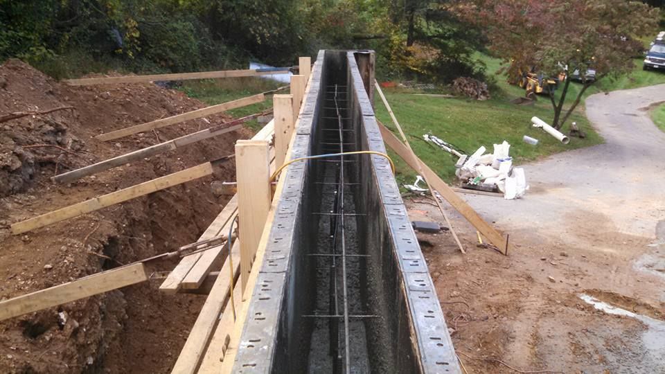 A view looking down a long, hollow concrete block wall under construction with steel rebar reinforcement installed inside.
