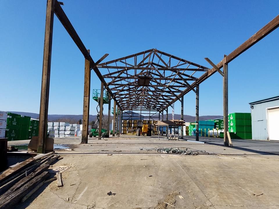 The metal framework of an open-air building structure stands over a concrete lot on a sunny day.
