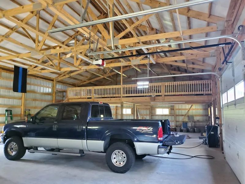 A dark blue pickup truck parked inside a large, wooden-framed pole barn with an open tailgate and overhead loft.