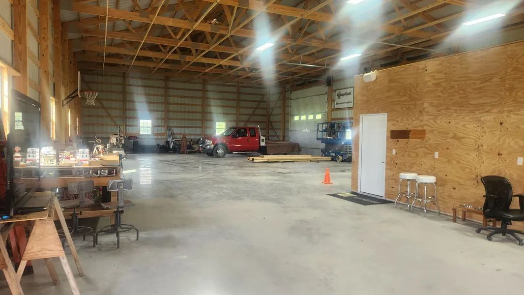 A large, open garage with concrete floors, exposed wooden ceiling beams, and a red truck parked in the back.