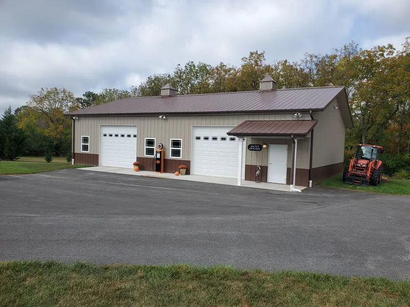 A tan metal building with two white garage doors, a brown roof, and an entrance canopy, set on an asphalt lot.