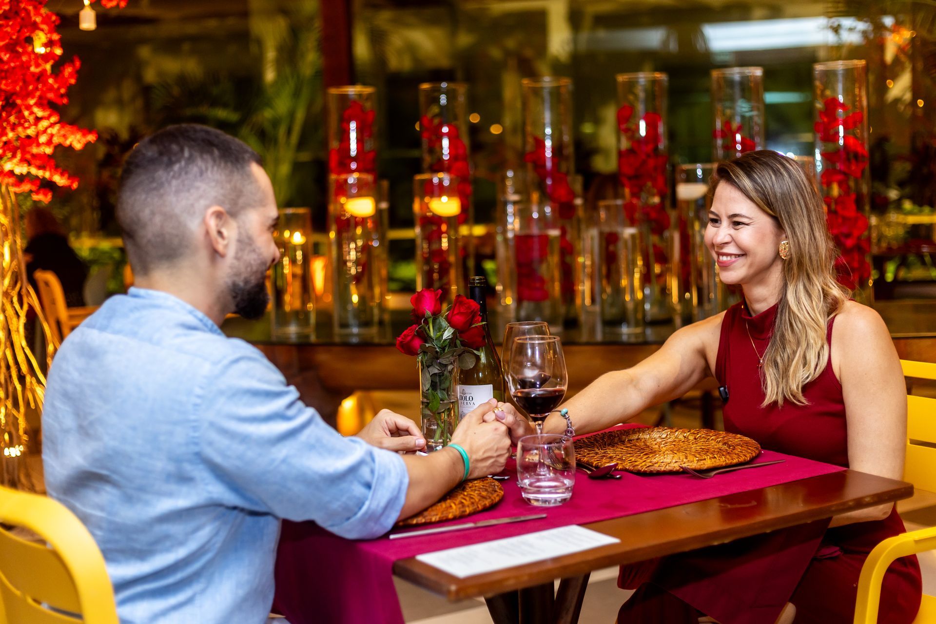 Casal sorrindo em cenário romântico no Kembali, com decoração vermelha e clima de Dia dos Namorados