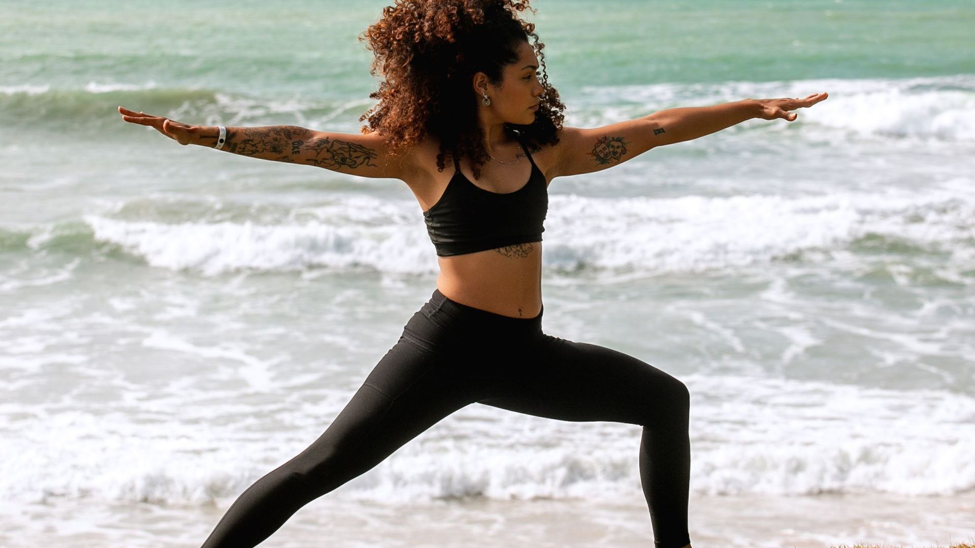 Professora de yoga fazendo a postura do guerreiro dois no deck do hotel, com o mar ao fundo.