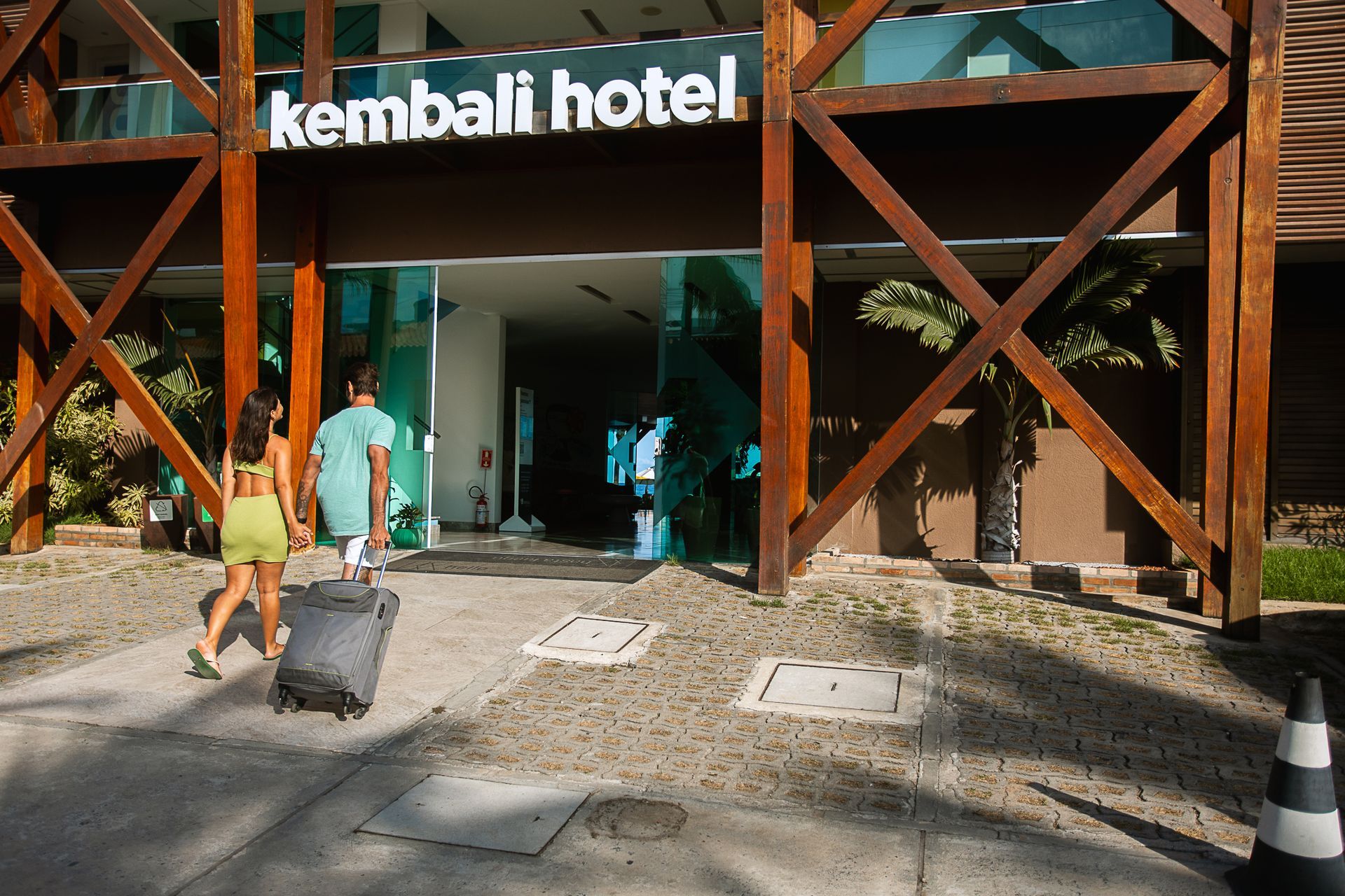 Casal de mãos dadas entrando no hotel com uma mala.