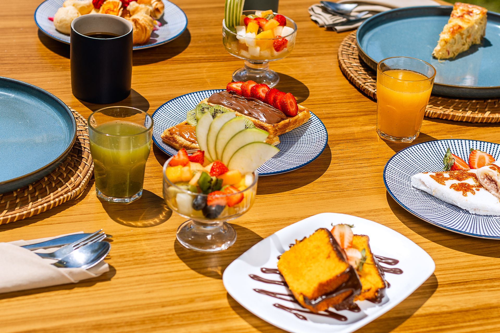 Mesa de café da manhã com frutas, sucos, bolos e doces em louça azul & branca.
