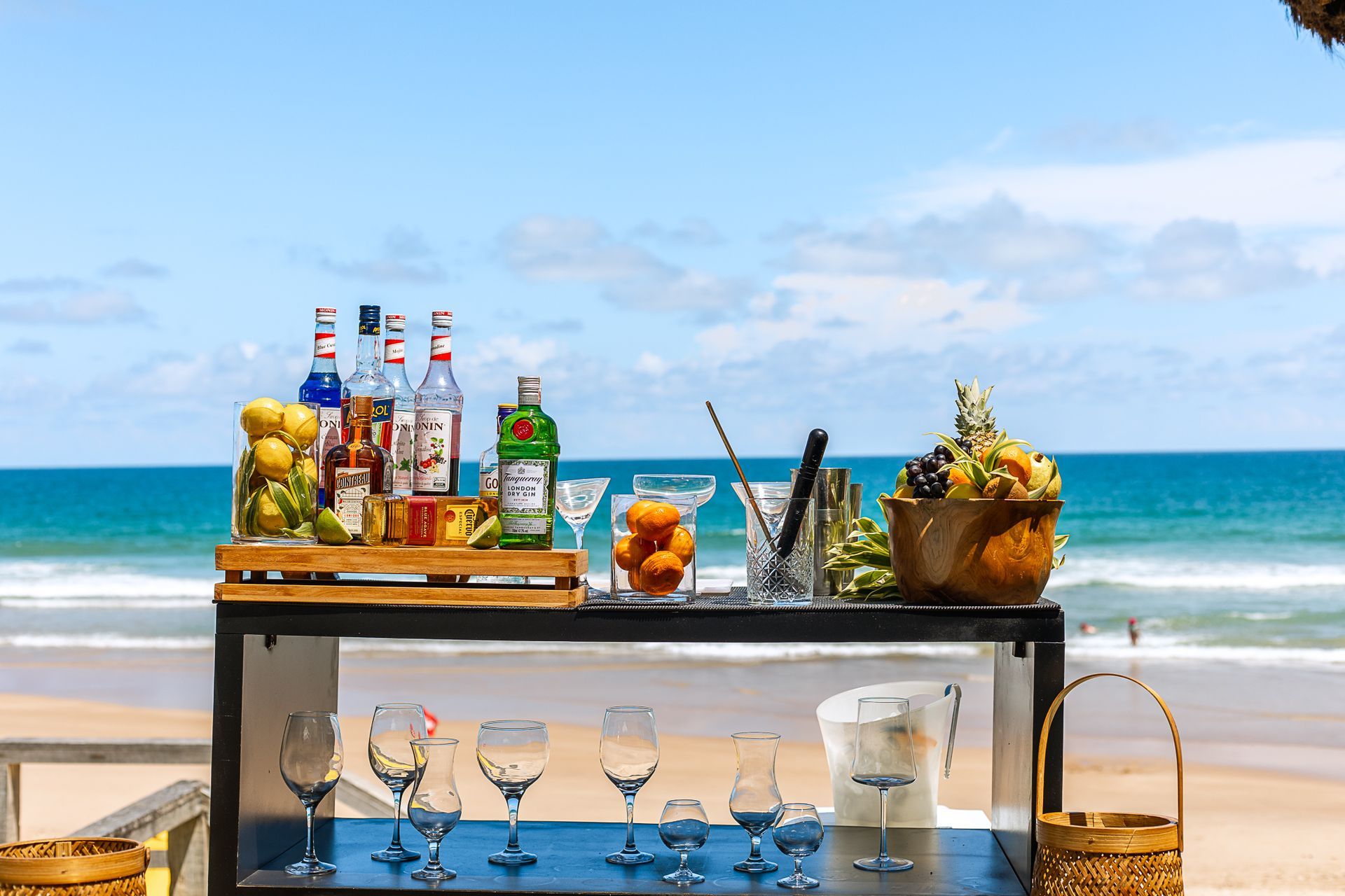 Bar de drinks completo à beira-mar, com frutas frescas, bebidas e utensílios de preparo.