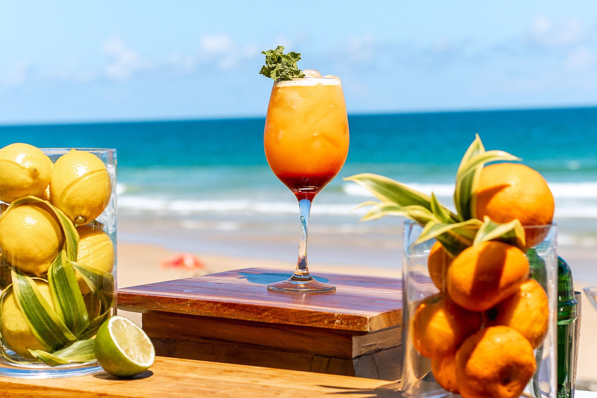 Aperol Spritz com frutas cítricas, servido à beira-mar, com cores vibrantes e clima tropical.