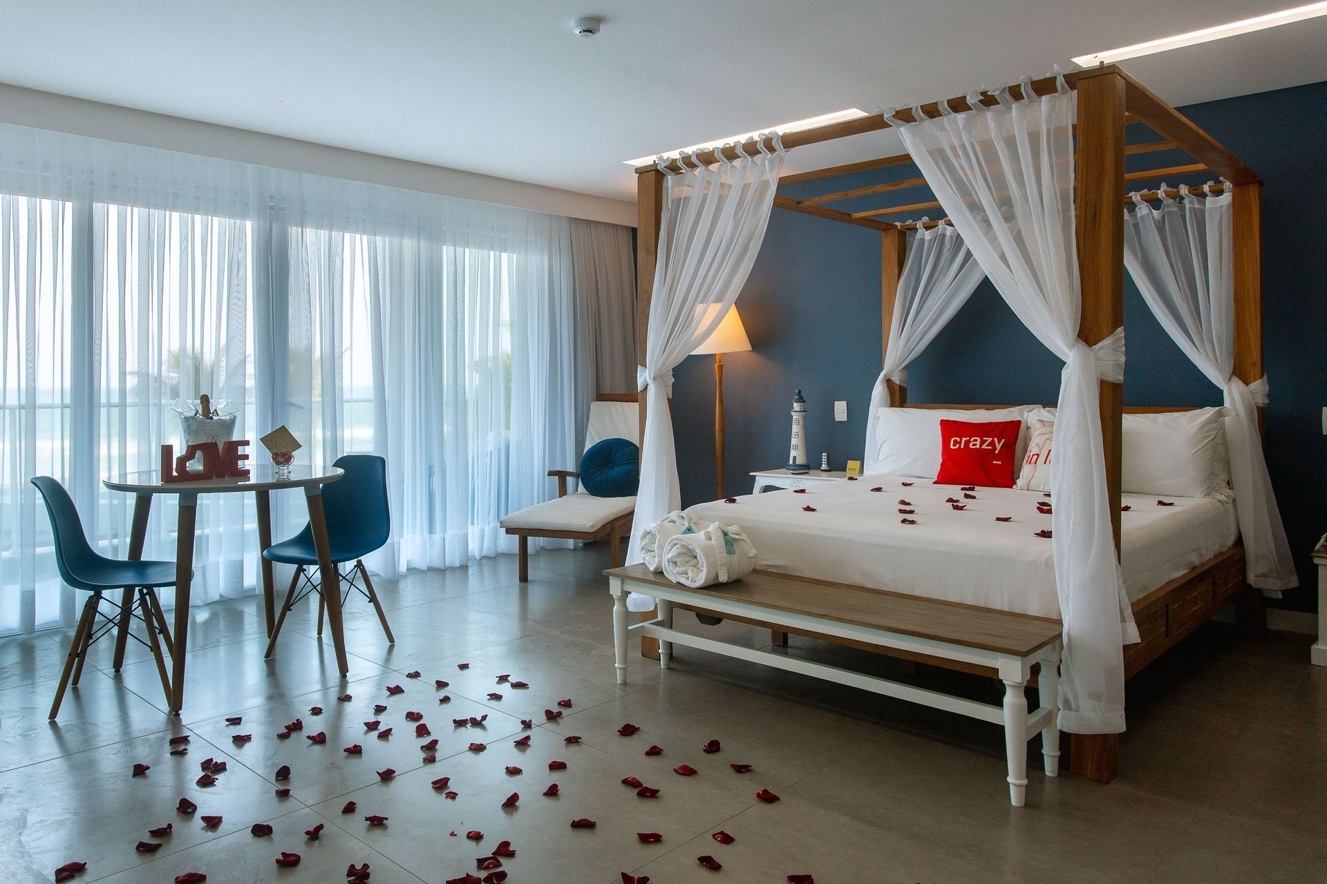 Quarto de hotel com decoração romântica, cama de dossel e pétalas de rosas pelo chão.
