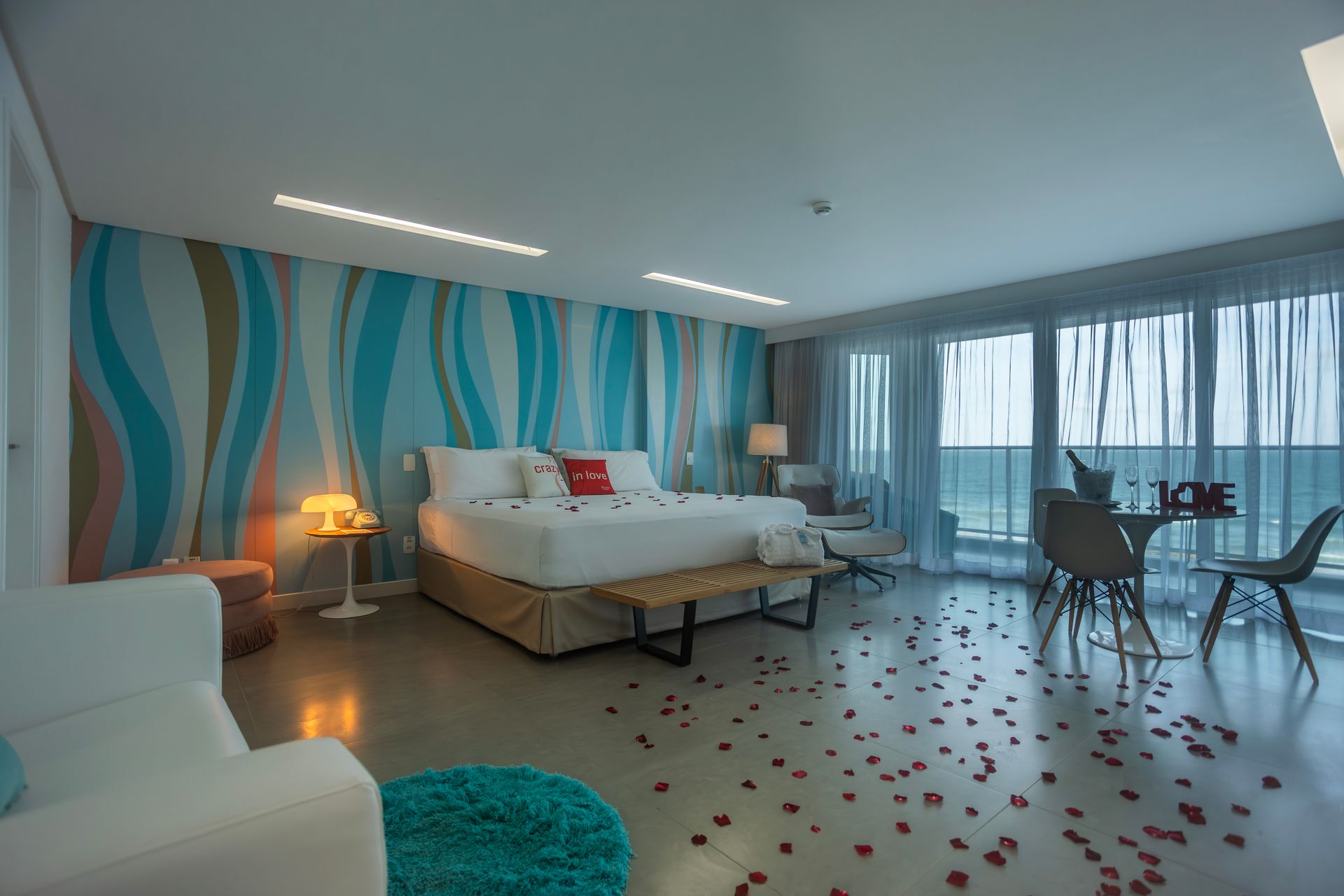 Quarto de hotel moderno com decoração romântica e pétalas de rosas espalhadas pelo chão.