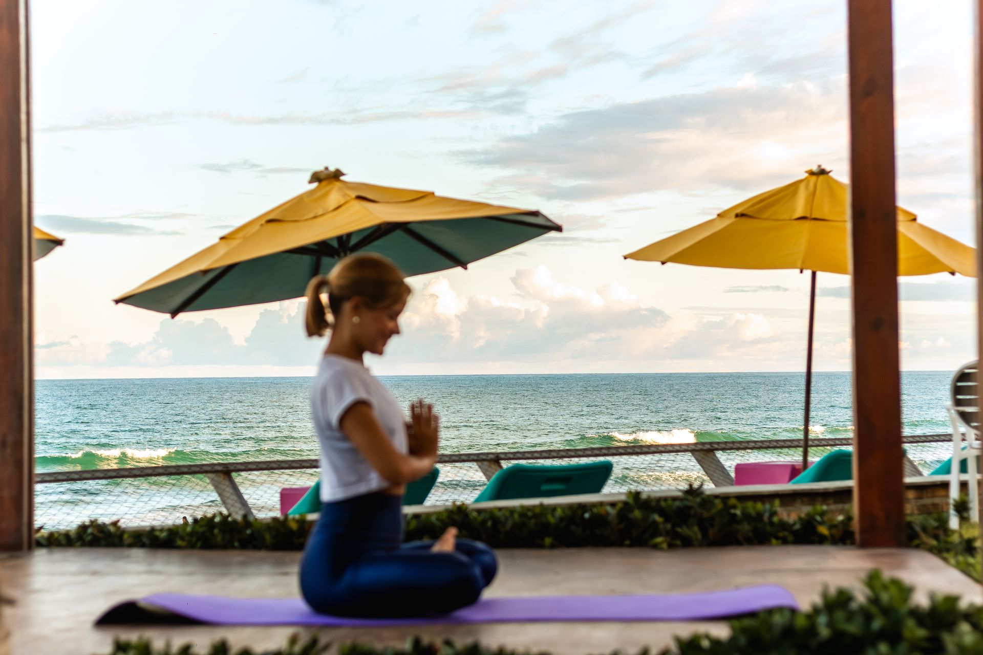 Mulher meditando em tapete de yoga com vista para o mar.