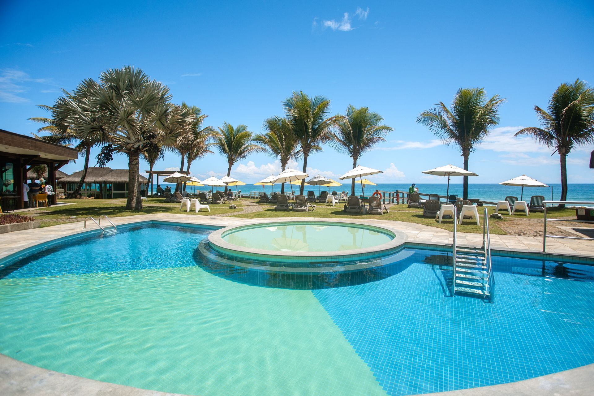 Piscina à beira-mar do Kembali com vista para a praia e área de descanso entre coqueiros.