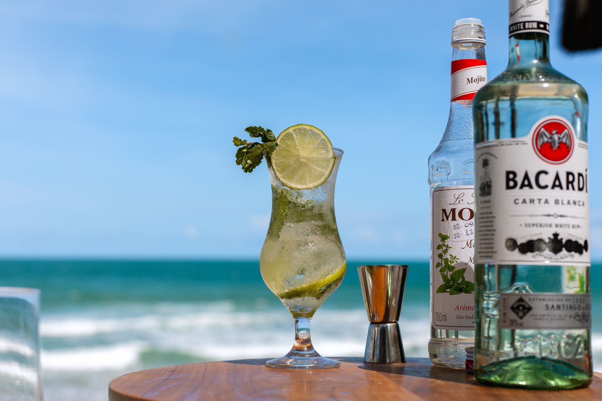 Mojito com limão e hortelã, servido à beira-mar, com o oceano ao fundo.