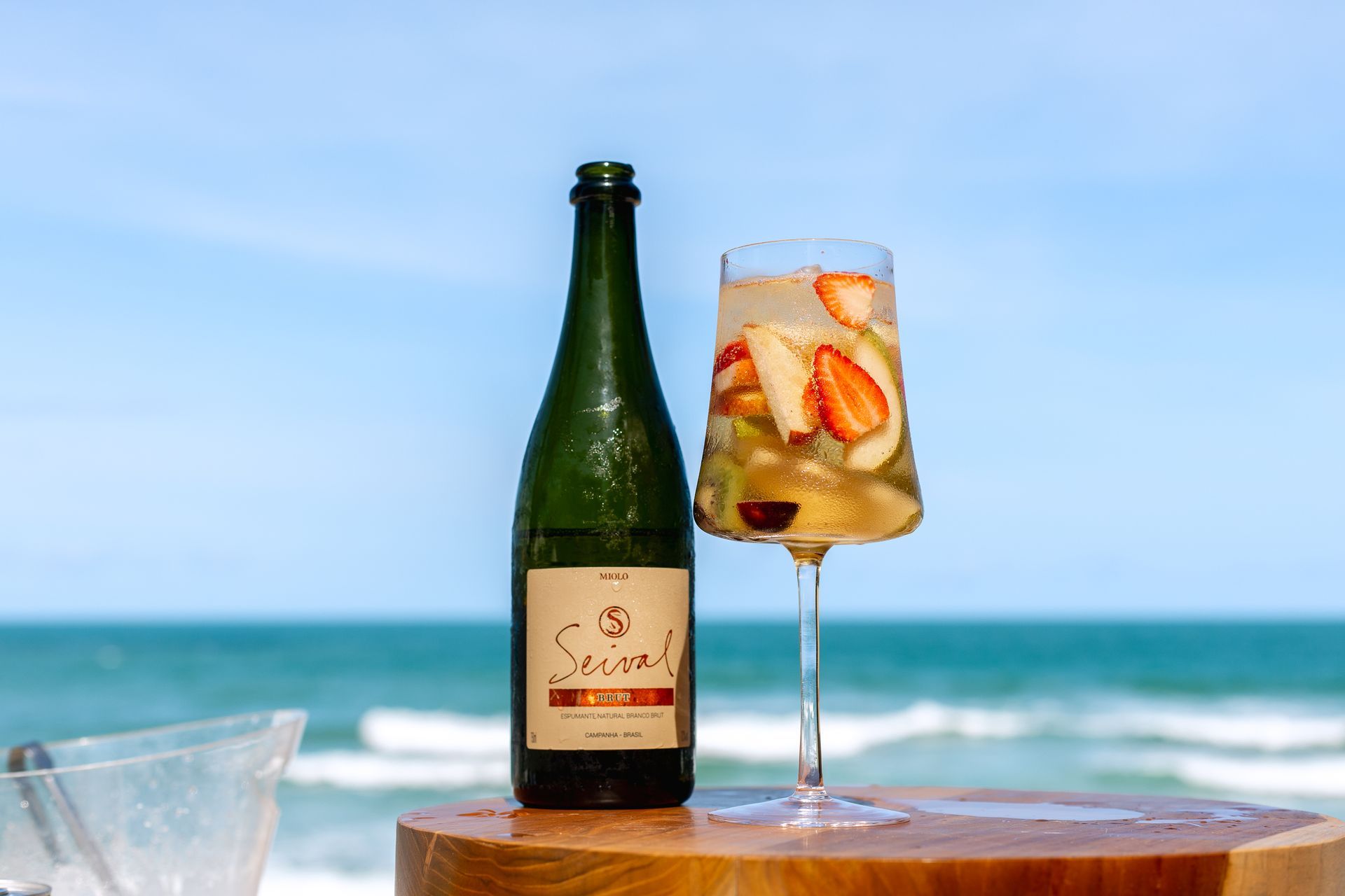 Clericot com frutas frescas e espumante, servido à beira-mar em um dia ensolarado.