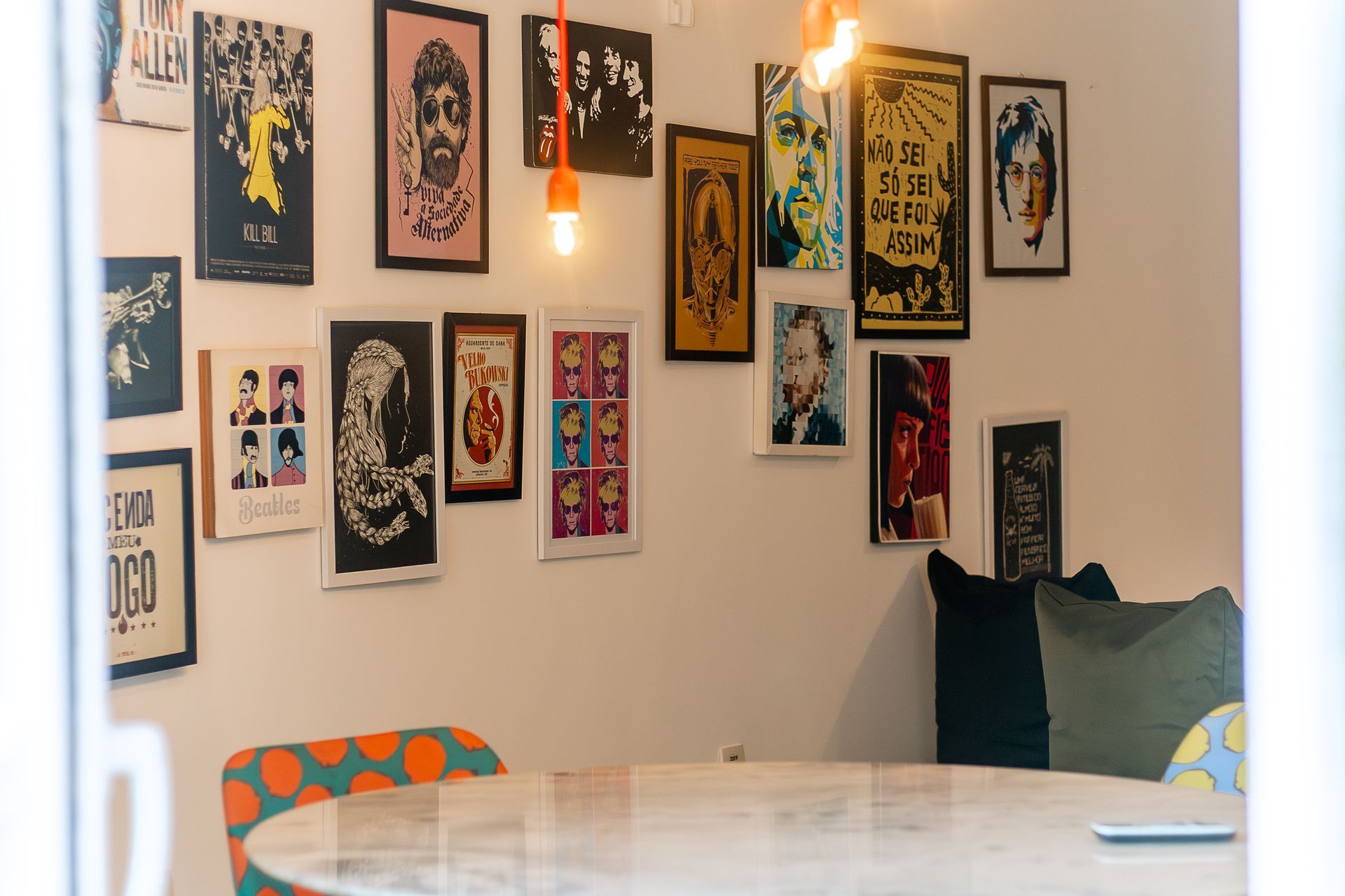 Sala living room com paredes brancas, posters de pop art, cadeira colorida & luminária em neon laranja.