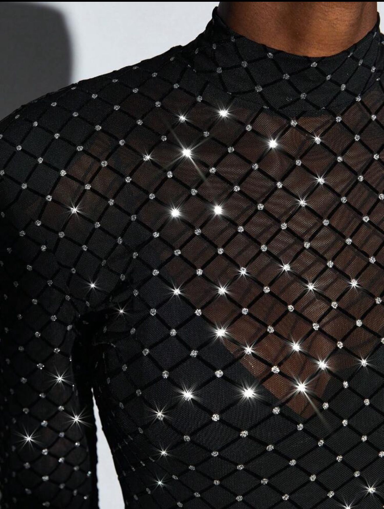 Primer plano de un top de malla negra brillante con mangas largas y escote alto.