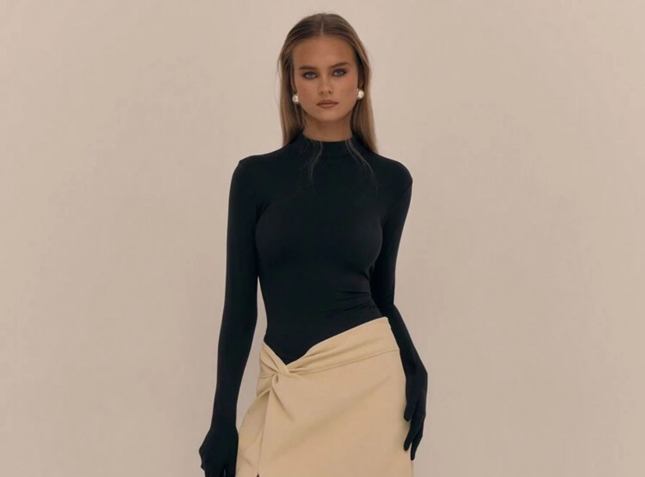 Una mujer lleva un top negro y una falda beige.