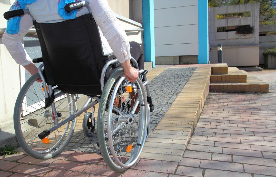 Person in wheelchair using a ramp to enter a building with blue and tan exterior.