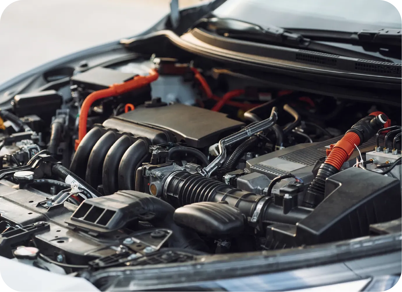 A close-up view of a car engine bay featuring black engine components and prominent high-voltage orange cables.