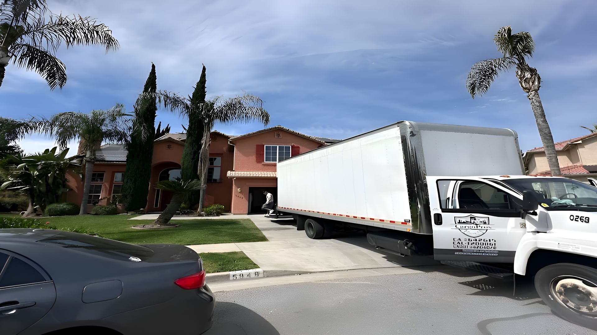Moving truck parked in front of a house. A car is on the left. Bright sunny day.