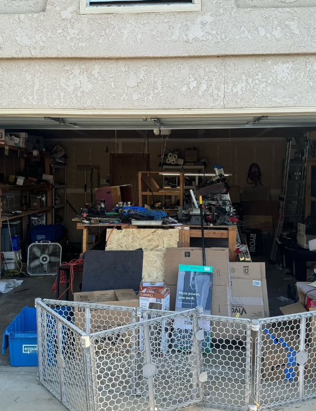 Open garage filled with clutter; a baby gate is in front of the garage door.