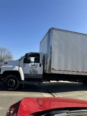 White moving truck on a sunny day with red car in foreground.