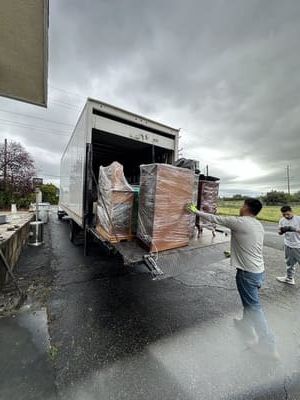 Men loading wrapped furniture onto a white truck on a wet day.