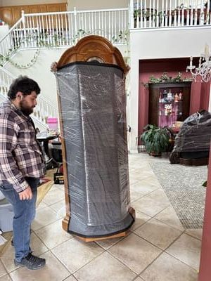 Man next to a tall, wrapped cabinet. Interior setting with staircase, tile floor, and other furniture.