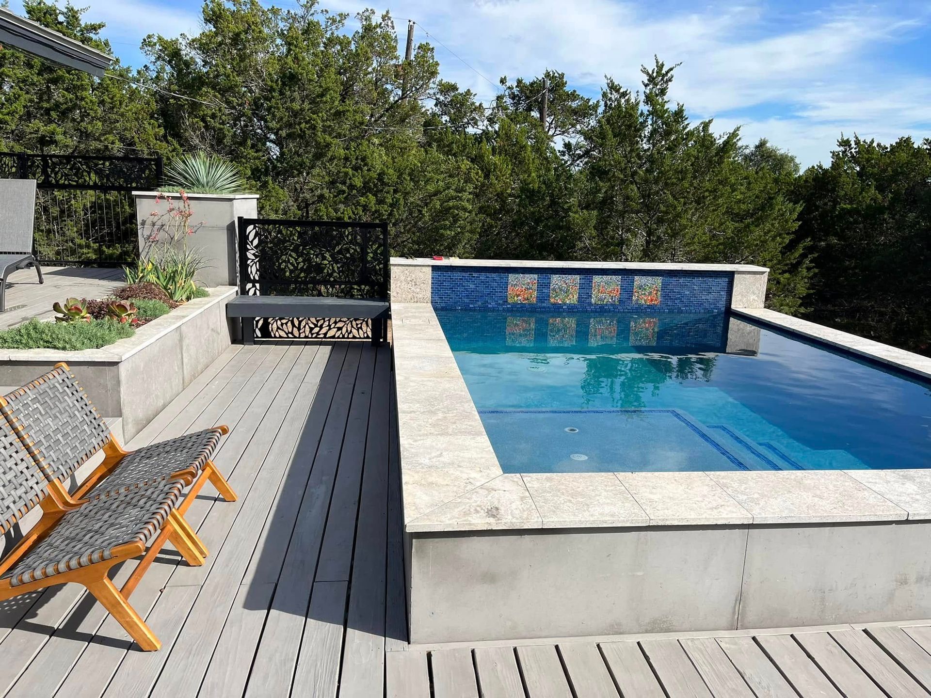 Modern backyard patio with a rectangular pool, gray deck, and lounge chairs in the sun
