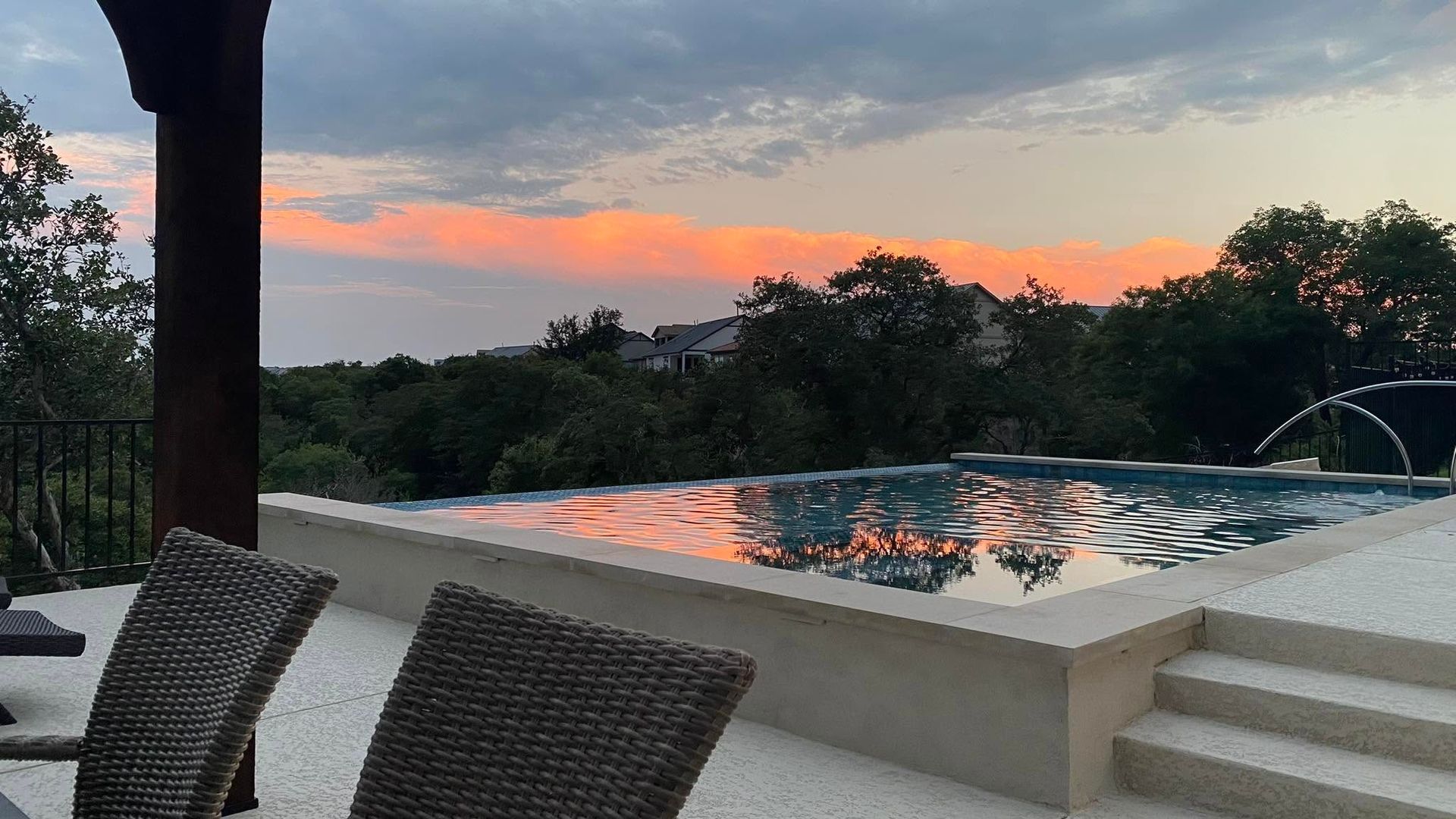 Backyard pool at sunset with lounge chairs, steps, and orange clouds reflecting on the water