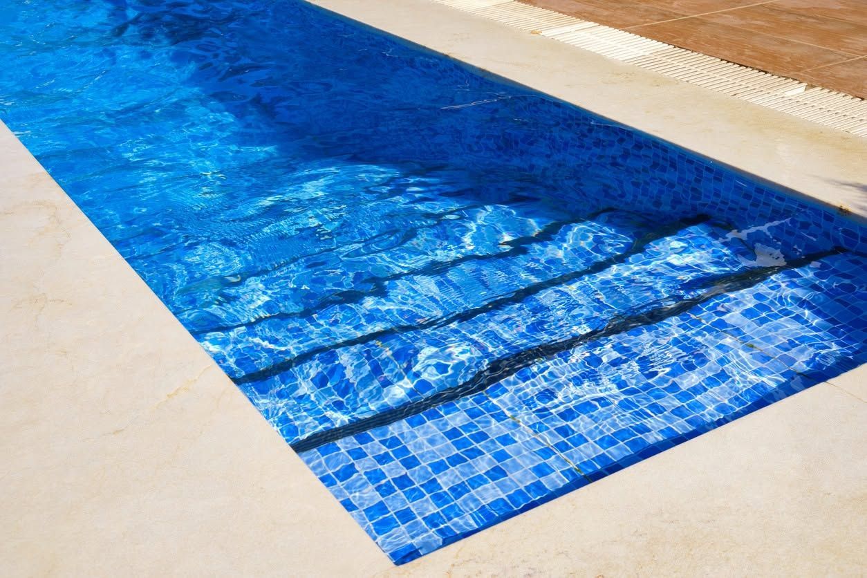 Blue swimming pool cover stretched over a pool beside beige tiles.