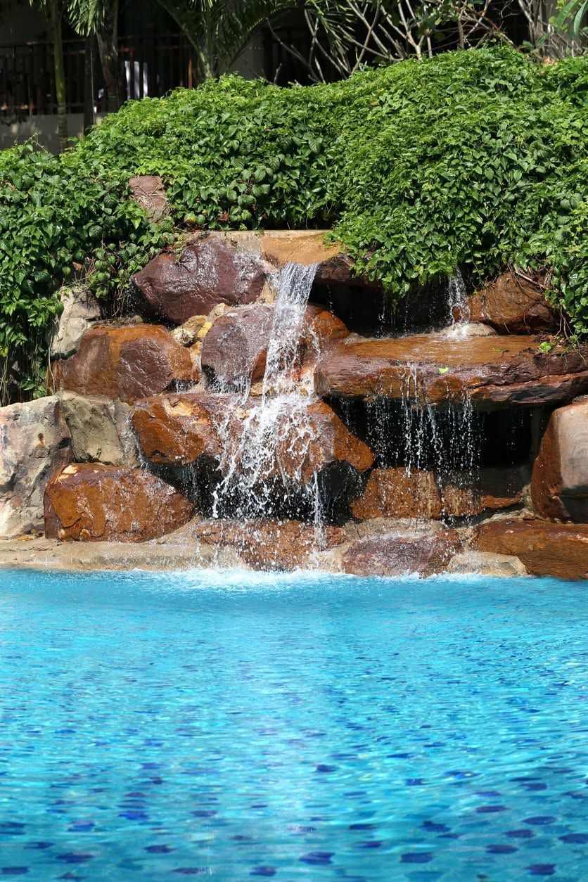 Pool waterfall with rocks and green foliage above bright blue water