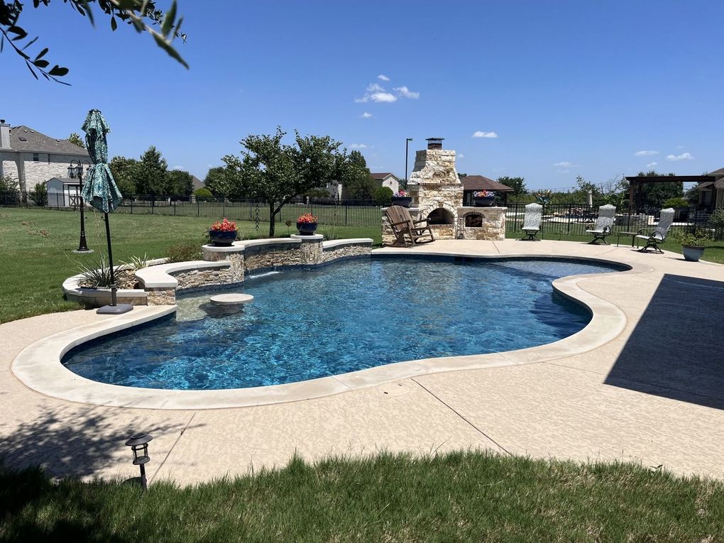 Backyard swimming pool with stone waterfall, lounge chairs, and a clear blue sky