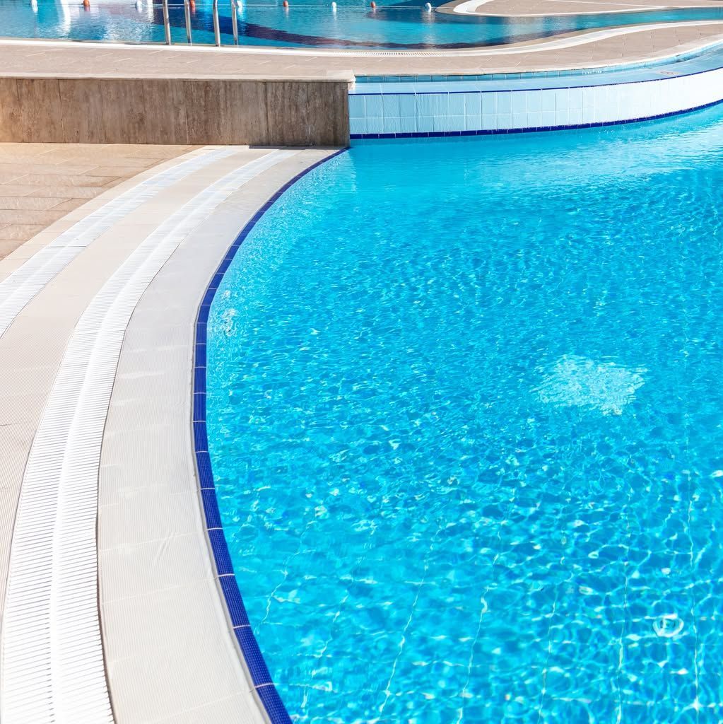 Curved turquoise swimming pool with white deck and blue water reflections