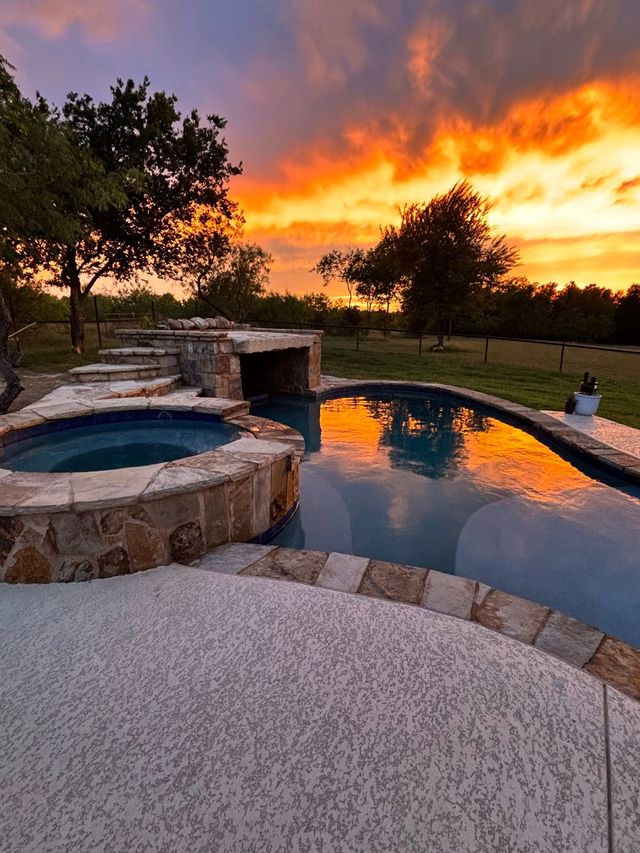 Sunset over a backyard pool and hot tub with orange sky reflecting on still water