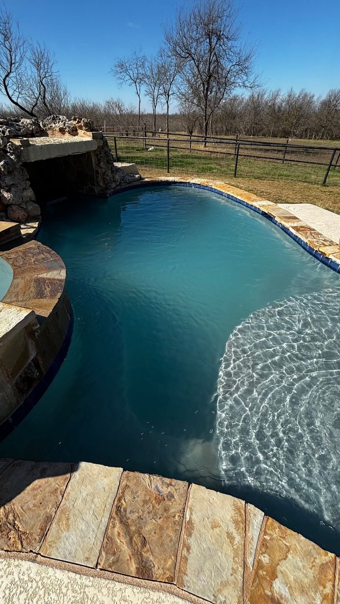 Backyard pool with stone edging, turquoise water, and a waterfall feature in a sunny desert setting
