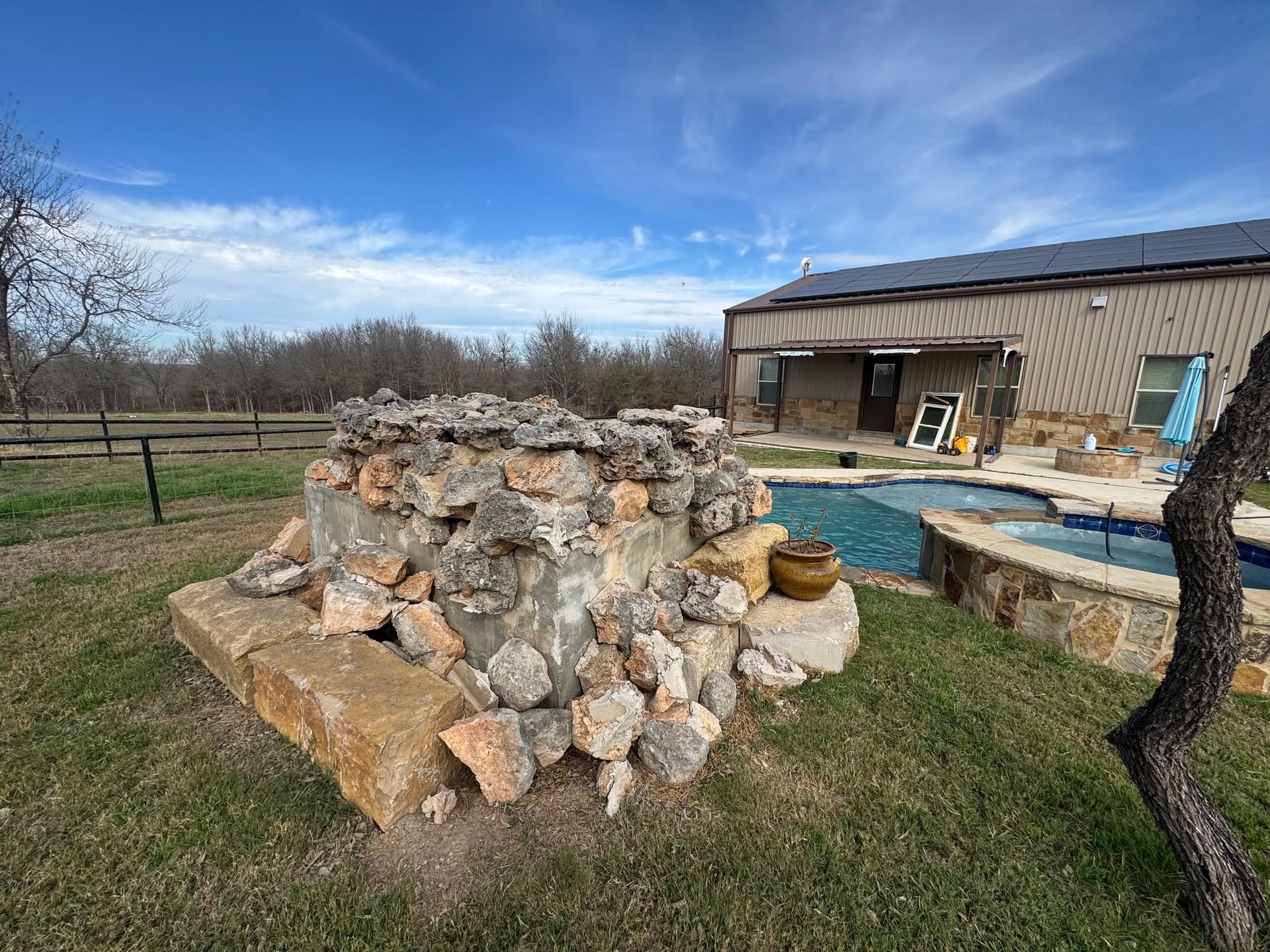 Backyard stone fire pit beside a patio and brick house under a blue sky