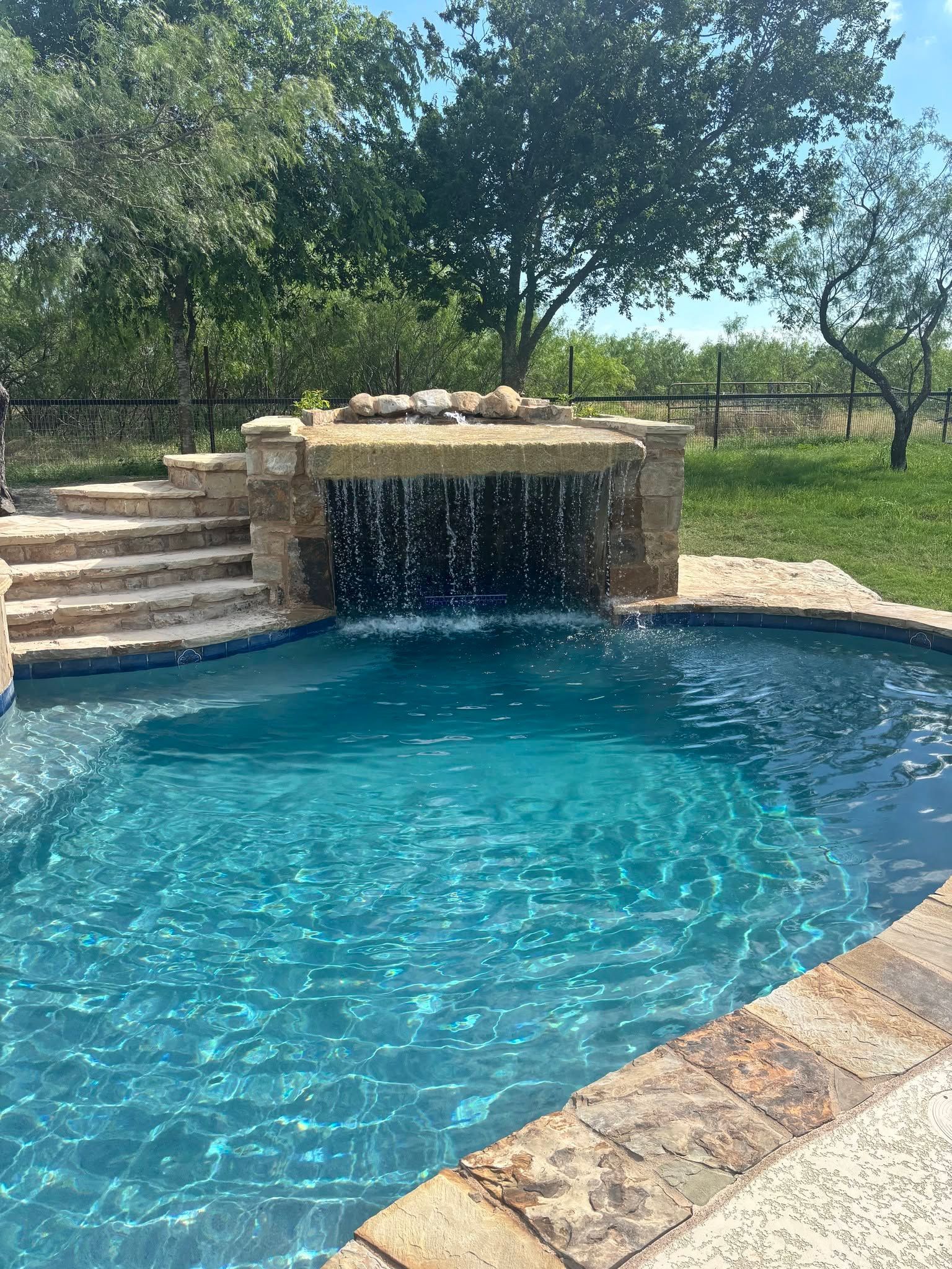 Blue pool with a stone waterfall, steps, and trees in the background