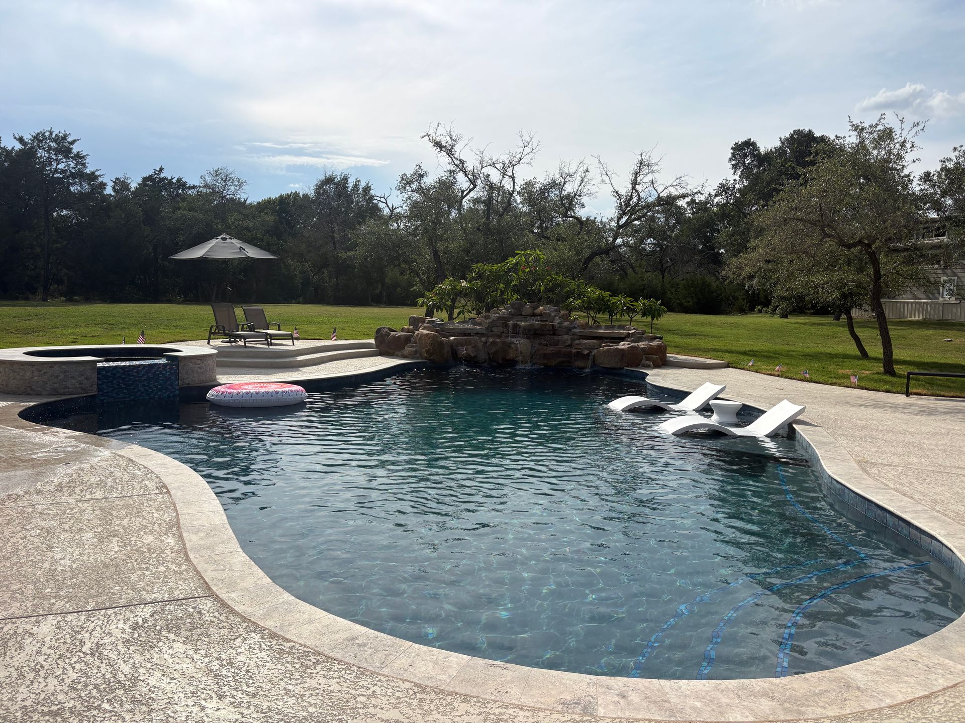 Curved backyard pool with lounge chairs, umbrella, and grassy yard in bright daylight