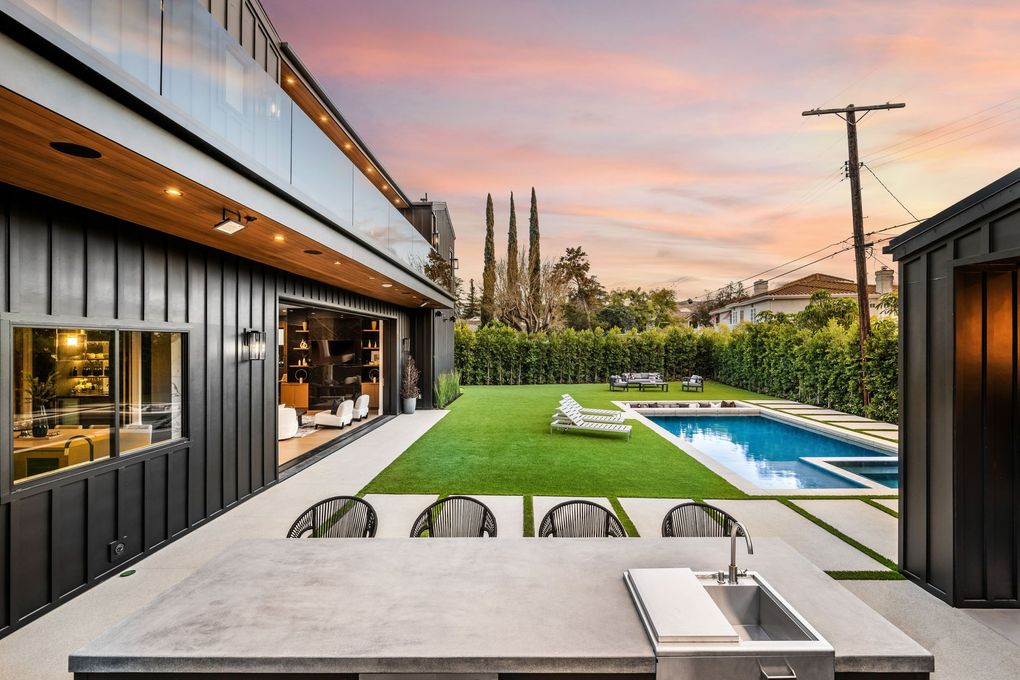 Modern backyard patio with pool, green lawn, lounge chairs, and contemporary house at sunset