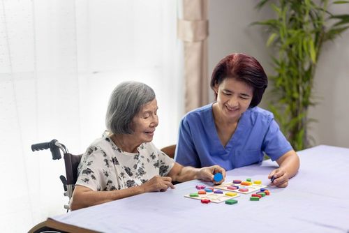 Caregiver and senior woman playing wooden shape puzzles game for dementia prevention