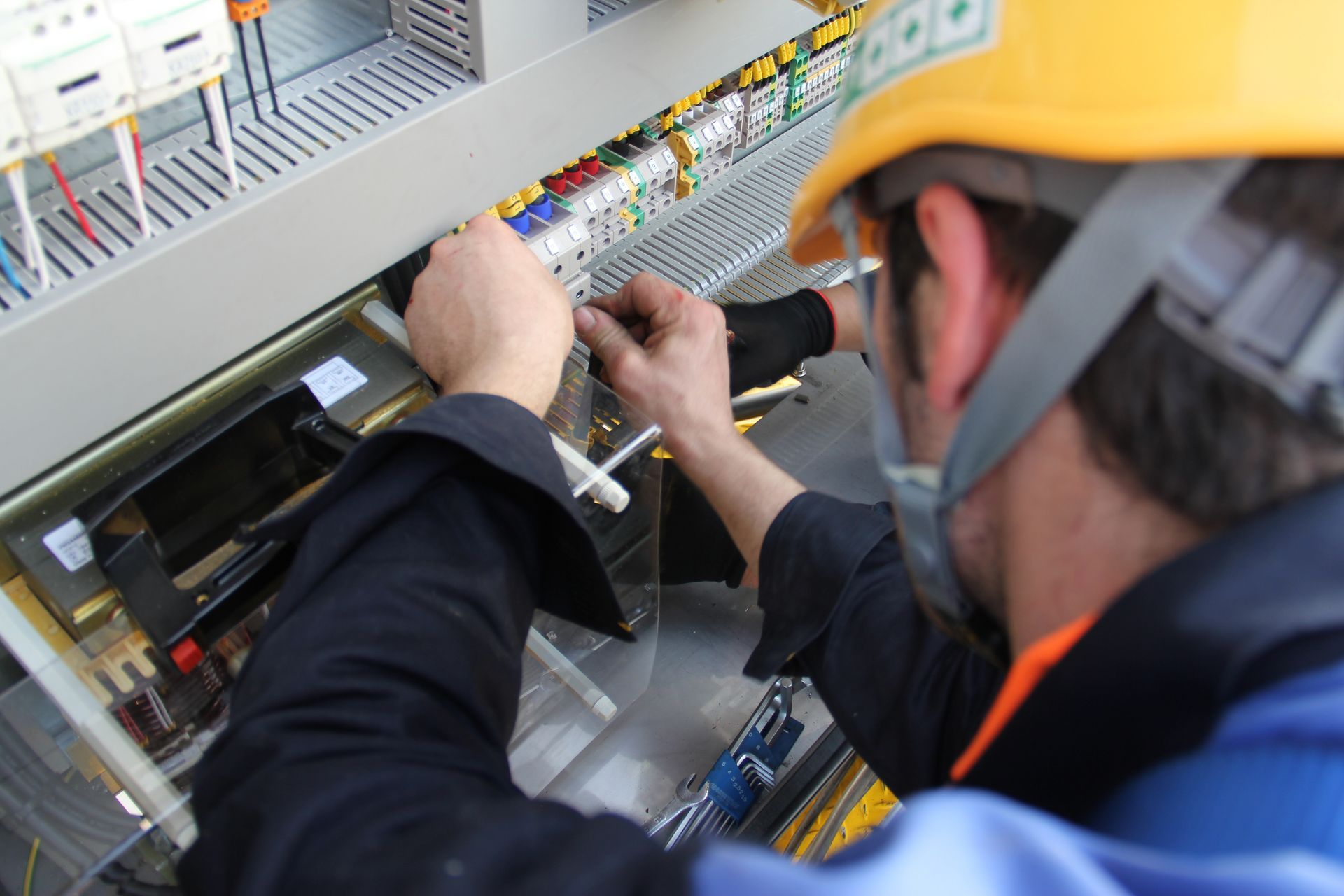 Tecnico al lavoro all'interno di un quadro elettrico, intento a regolare fili e componenti indossando un elmetto protettivo.