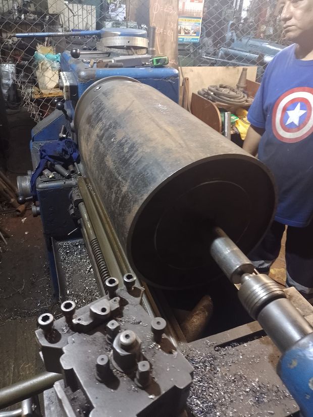 Un trabajador maneja un torno de metal sobre una gran pieza cilíndrica de acero en un taller.
