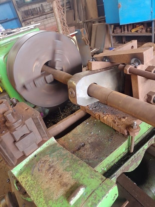 Torno de metal mecanizando una gran pieza cilíndrica en un taller, con bancada verde y soportes de madera.