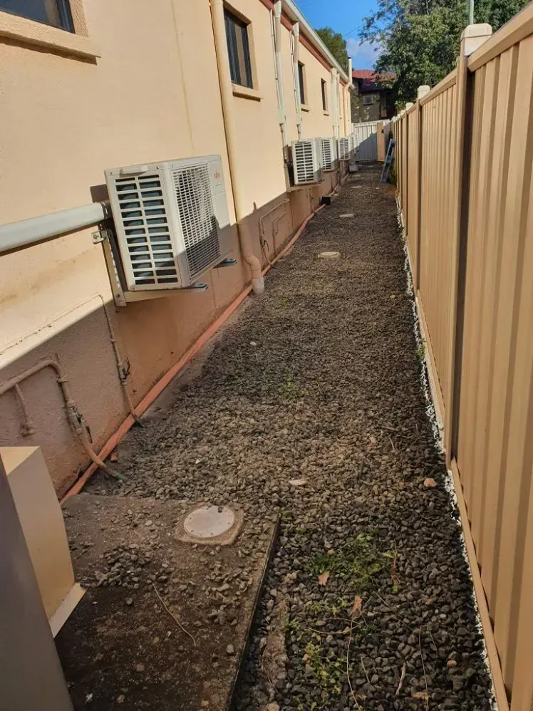 Narrow Gravel Path Between a Building and a Tan Fence — Dominion Pest Control in Kingaroy, QLD