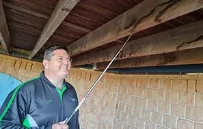 Man Inspecting Wooden Beams With a Long Pole Under a Brick Structure — Dominion Pest Control in Kingaroy, QLD