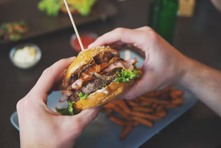 A person is eating a hamburger with a toothpick in it.