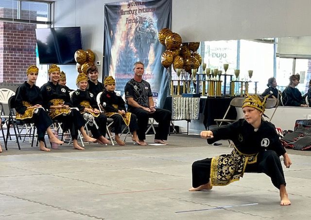 A group of people are sitting in chairs watching a young boy perform martial arts.
